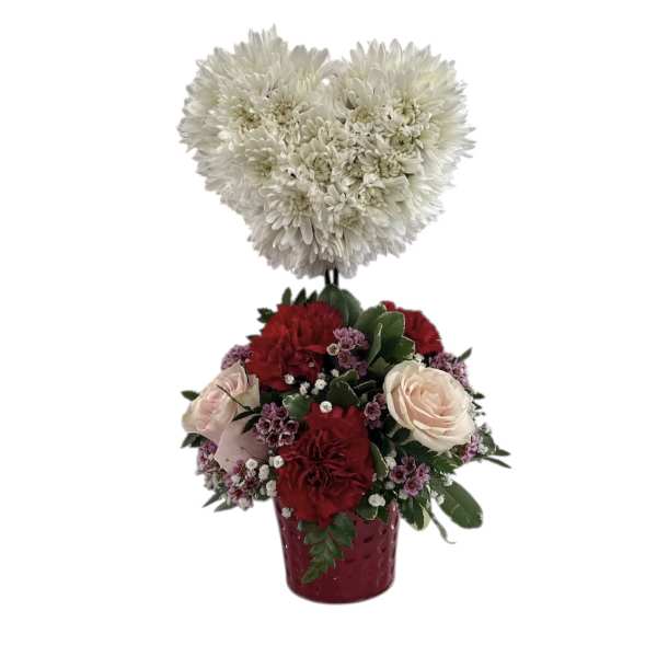 Heart-shaped white chrysanthemum topper above a red and blush rose arrangement in a vase