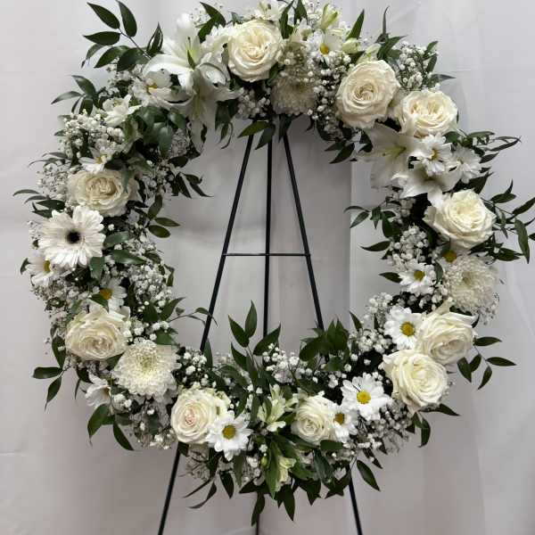 White floral wreath on a black stand with roses and daisies