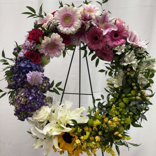 Large floral wreath with pink, purple, white, and yellow blooms on a black stand