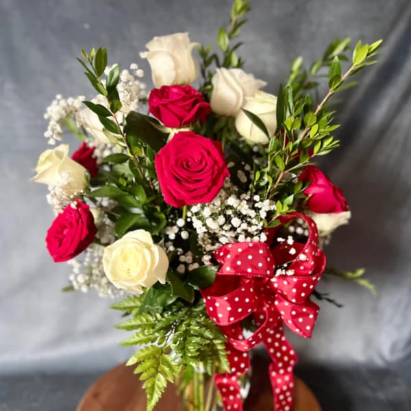 Bouquet of red and white roses with baby's breath and a red polka-dot ribbon in a glass vase