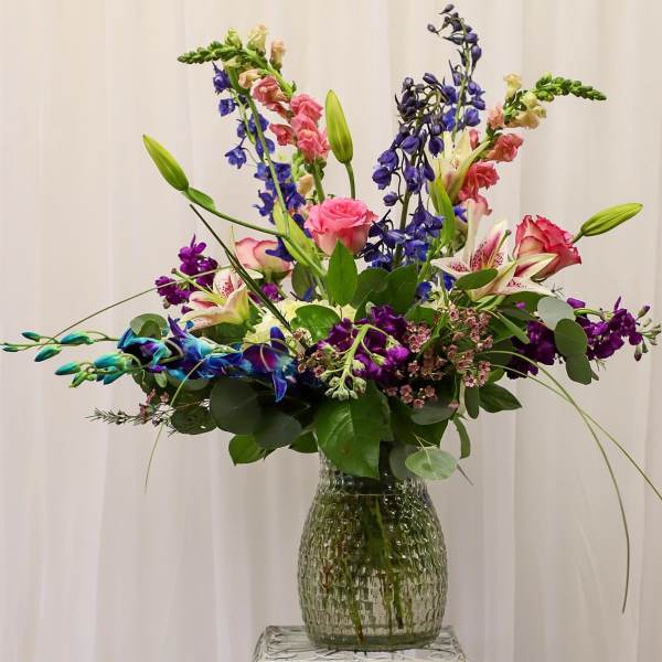 Tall mixed bouquet with lilies, roses, and purple blooms in a glass vase