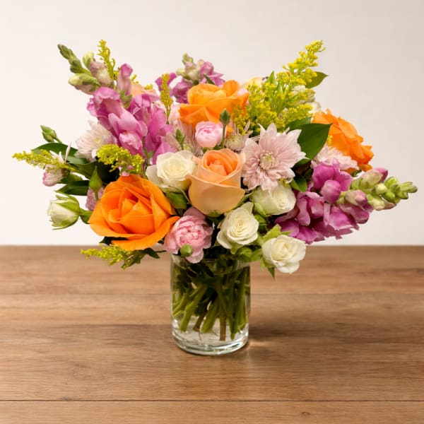 Mixed bouquet of orange, pink, and white flowers in a clear glass vase