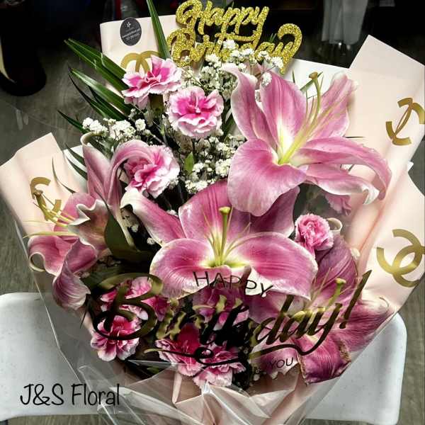 Pink lilies and carnations in a wrapped bouquet with a birthday topper
