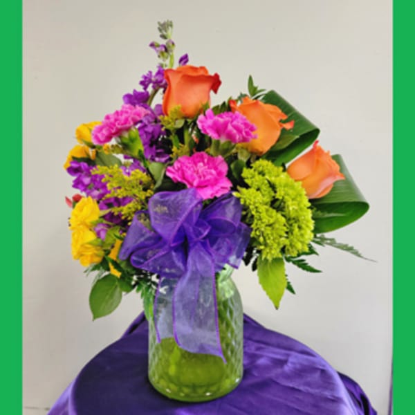 Colorful bouquet of roses and carnations in a glass vase with a purple ribbon
