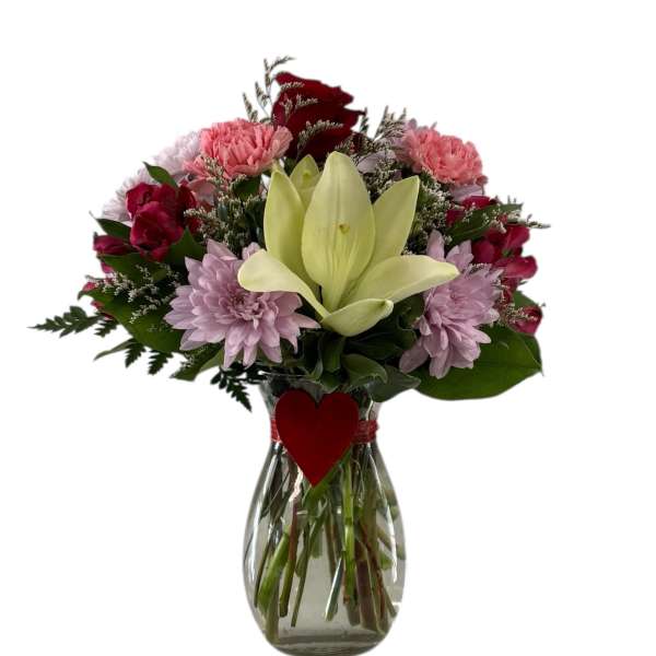 Bouquet of mixed pink and red flowers in a glass vase with a heart tag