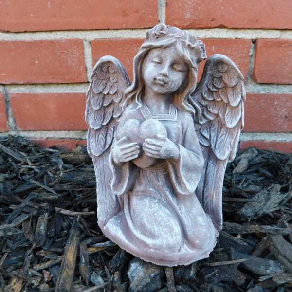 Stone angel figurine holding a heart in front of a brick wall