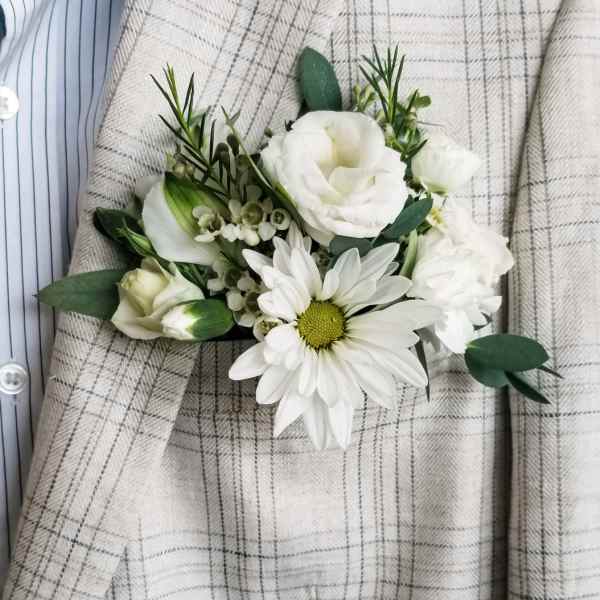 White boutonniere with daisy and rose blooms on a plaid jacket