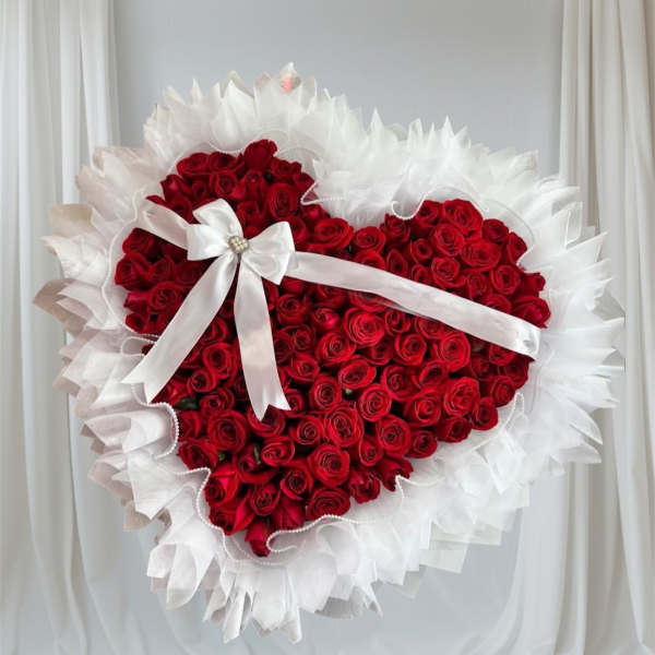 Heart-shaped bouquet of red roses with a white ribbon and ruffled white wrap