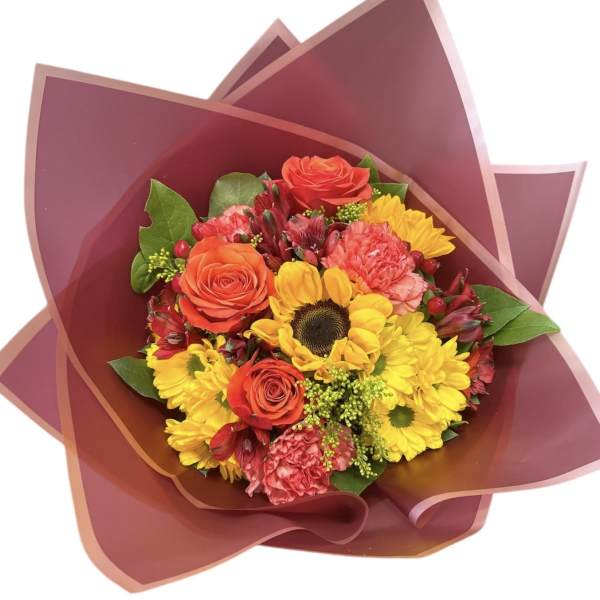 Bouquet of yellow daisies, orange roses, and pink carnations wrapped in burgundy paper