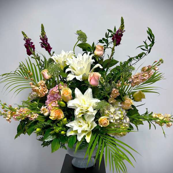 Tall floral arrangement with white lilies, peach roses, and purple spikes in a vase