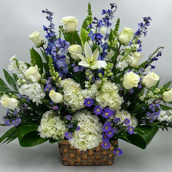 Large basket arrangement with white roses, hydrangeas, lilies, and purple flowers