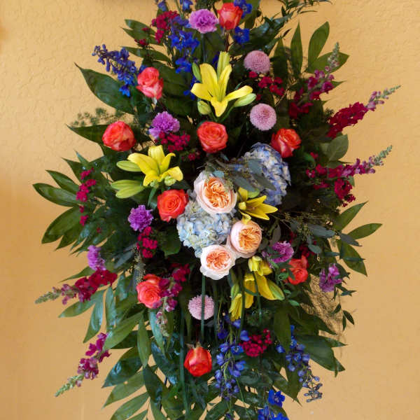 Tall standing floral spray with roses, lilies, and blue blossoms