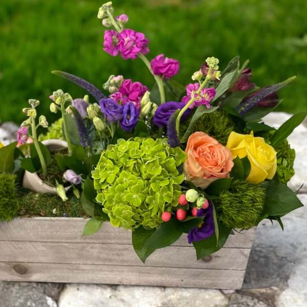 Mixed floral arrangement in a wooden box with bright pink, purple, yellow, and peach blooms