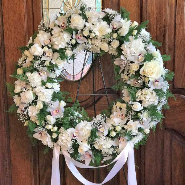 Large white floral wreath on a stand with a ribbon bow