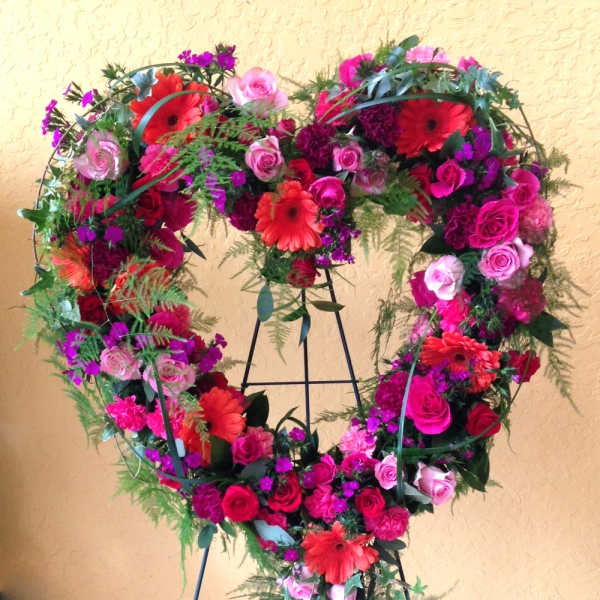 Heart-shaped floral wreath with pink and red flowers on a stand