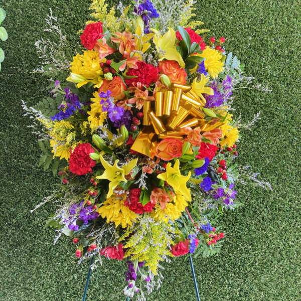 Colorful standing floral spray with a gold ribbon on a grassy background