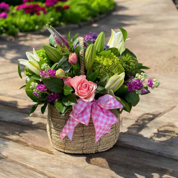Pink and white floral arrangement in a woven basket with a gingham bow