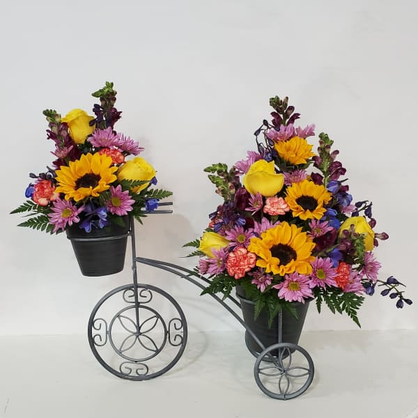 Two colorful flower arrangements in black pots on a decorative metal stand.