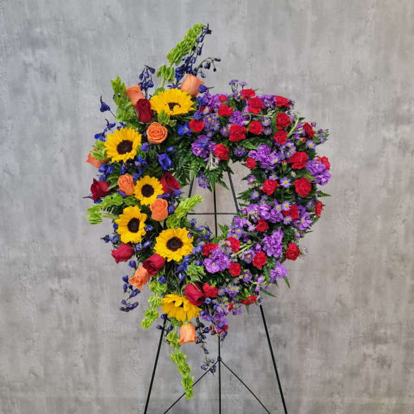 Heart-shaped floral wreath on a stand with sunflowers, roses, and purple blooms
