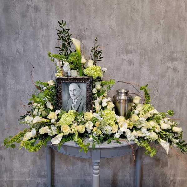 Sympathy floral tribute with a framed portrait and urn surrounded by white flowers