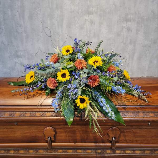 Large floral spray with sunflowers and orange blooms on a casket