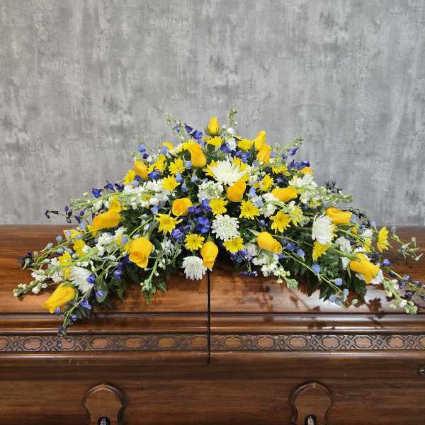 Large yellow, white, and blue floral spray on a wooden casket