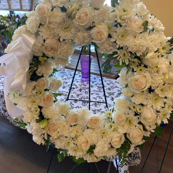 White floral wreath on a stand with roses and daisies