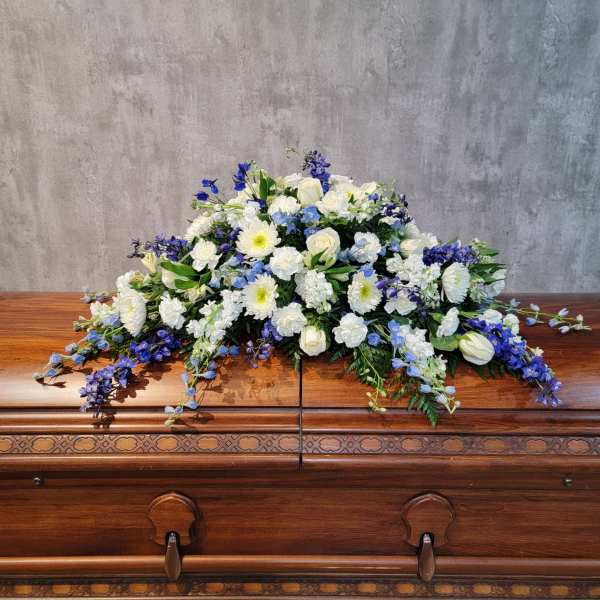 White and blue floral casket spray on a wooden casket