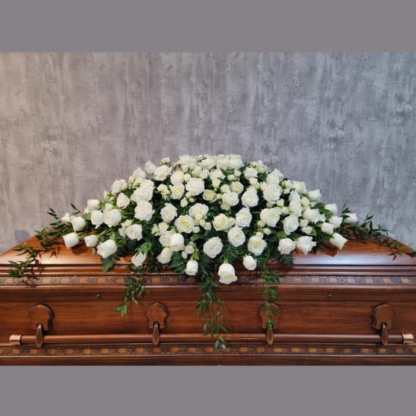 White rose casket spray with trailing greenery on a wooden casket