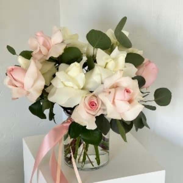 Bouquet of pale pink and white roses in a glass vase with a pink ribbon