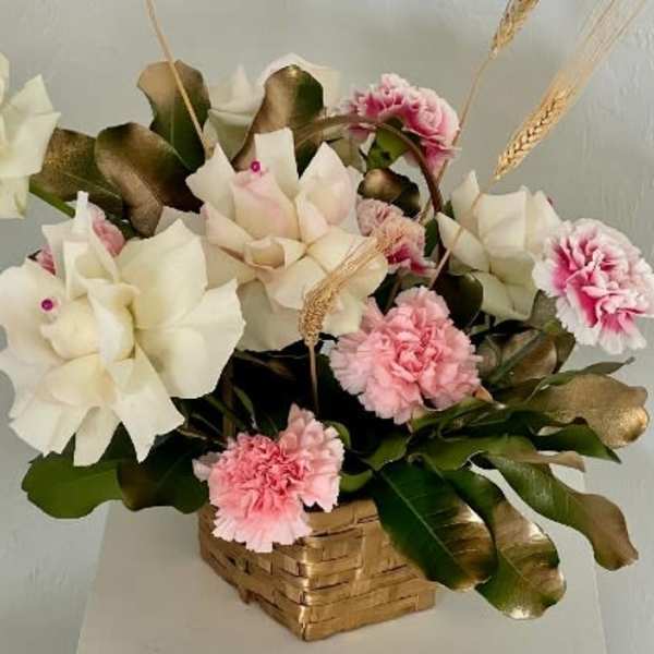 Pink and white floral arrangement in a woven basket with wheat stems