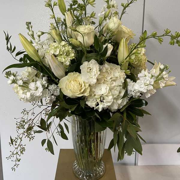 White floral arrangement in a clear glass vase with lilies and roses