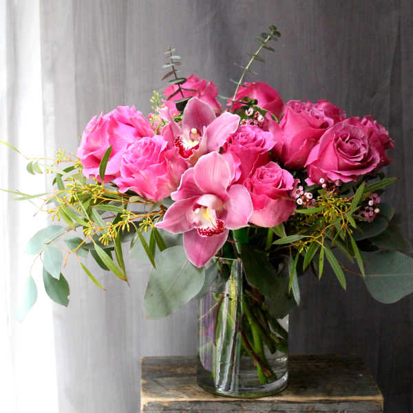 Pink roses and orchids arranged in a clear glass vase