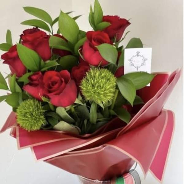 Bouquet of red roses with green accents wrapped in pink paper