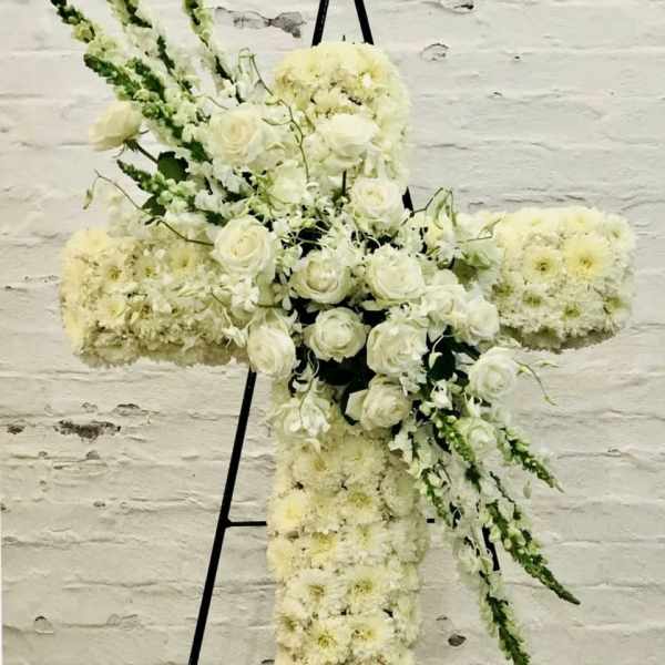 White floral cross arrangement on a black stand
