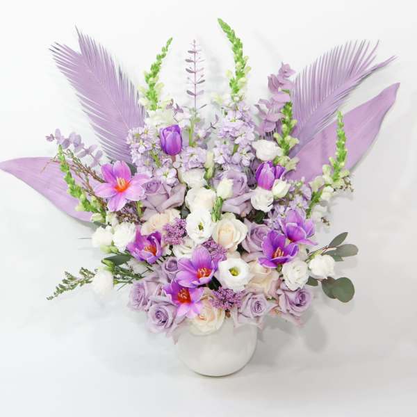 Lavender and purple floral arrangement in a white vase with decorative feathers