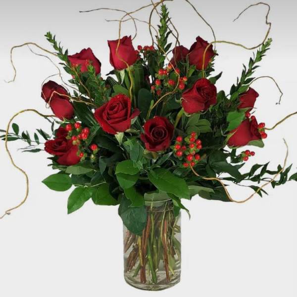 Red roses arranged in a clear glass vase with greenery and berry accents