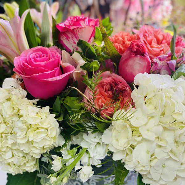 Low arrangement of bright pink roses, white hydrangeas, and coral blooms in a patterned container