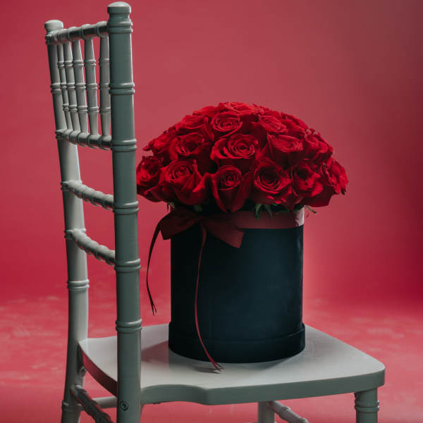 Red rose arrangement in a black hat box on a chair