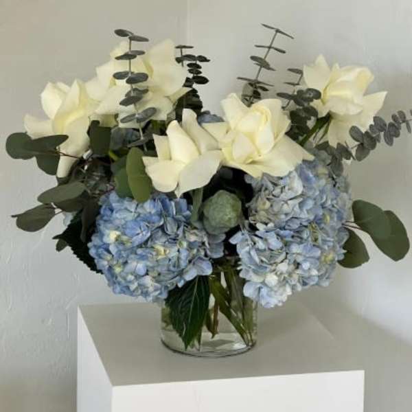 Blue hydrangeas and white flowers in a clear glass vase