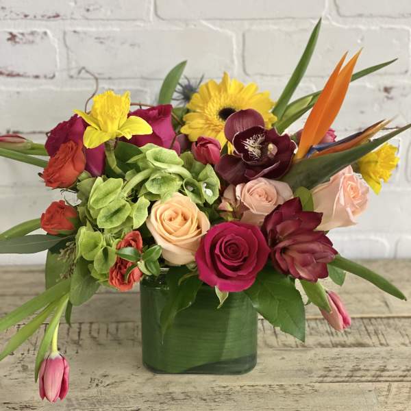 Mixed bouquet of roses, orchids, and bright tropical flowers in a green vase