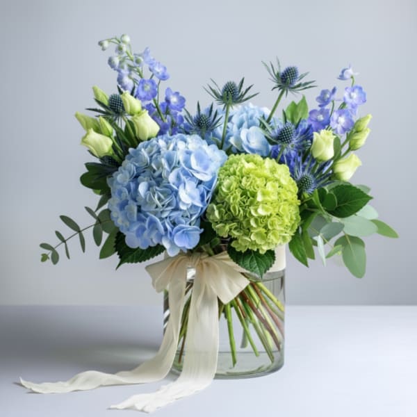 Blue and green floral arrangement in a glass vase with a ribbon