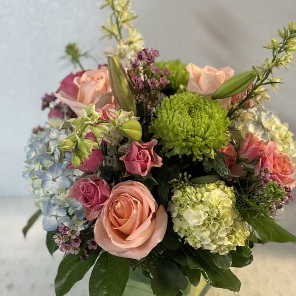 Mixed bouquet of pink roses, hydrangeas, and green chrysanthemums in a glass vase
