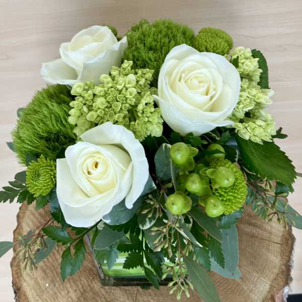 White roses and green flowers arranged in a square glass vase