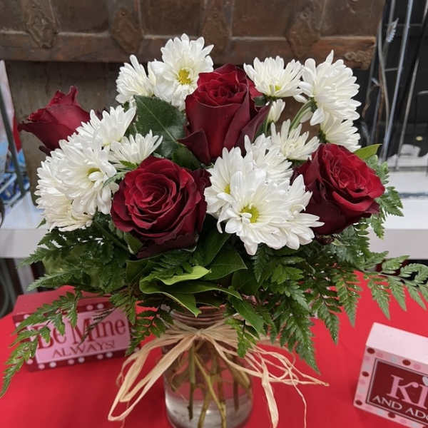 Red roses and white daisies in a glass vase with a raffia bow