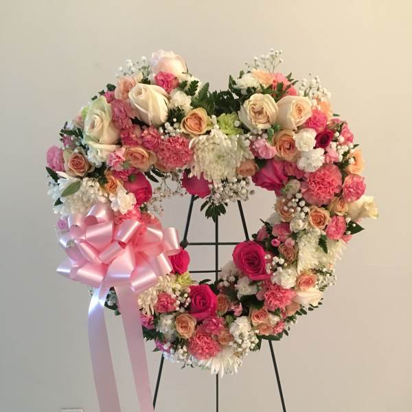 Heart-shaped floral wreath with pink and cream roses and a large pink ribbon