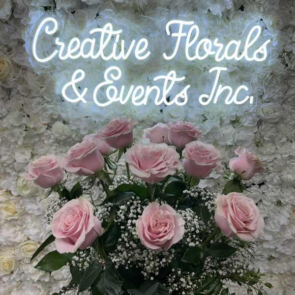 Pink roses arranged in front of a white floral wall with a glowing sign.