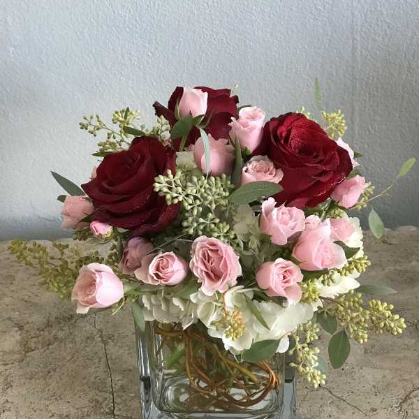 Pink and red roses arranged in a clear square vase