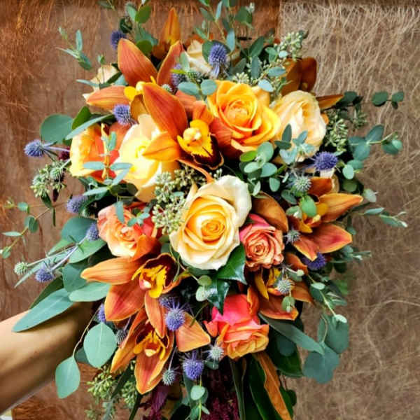 Bouquet of orange and cream roses with orange orchids and blue thistle