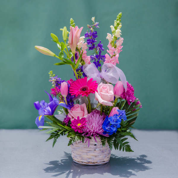 Mixed bouquet in a woven basket with pink, purple, and blue flowers